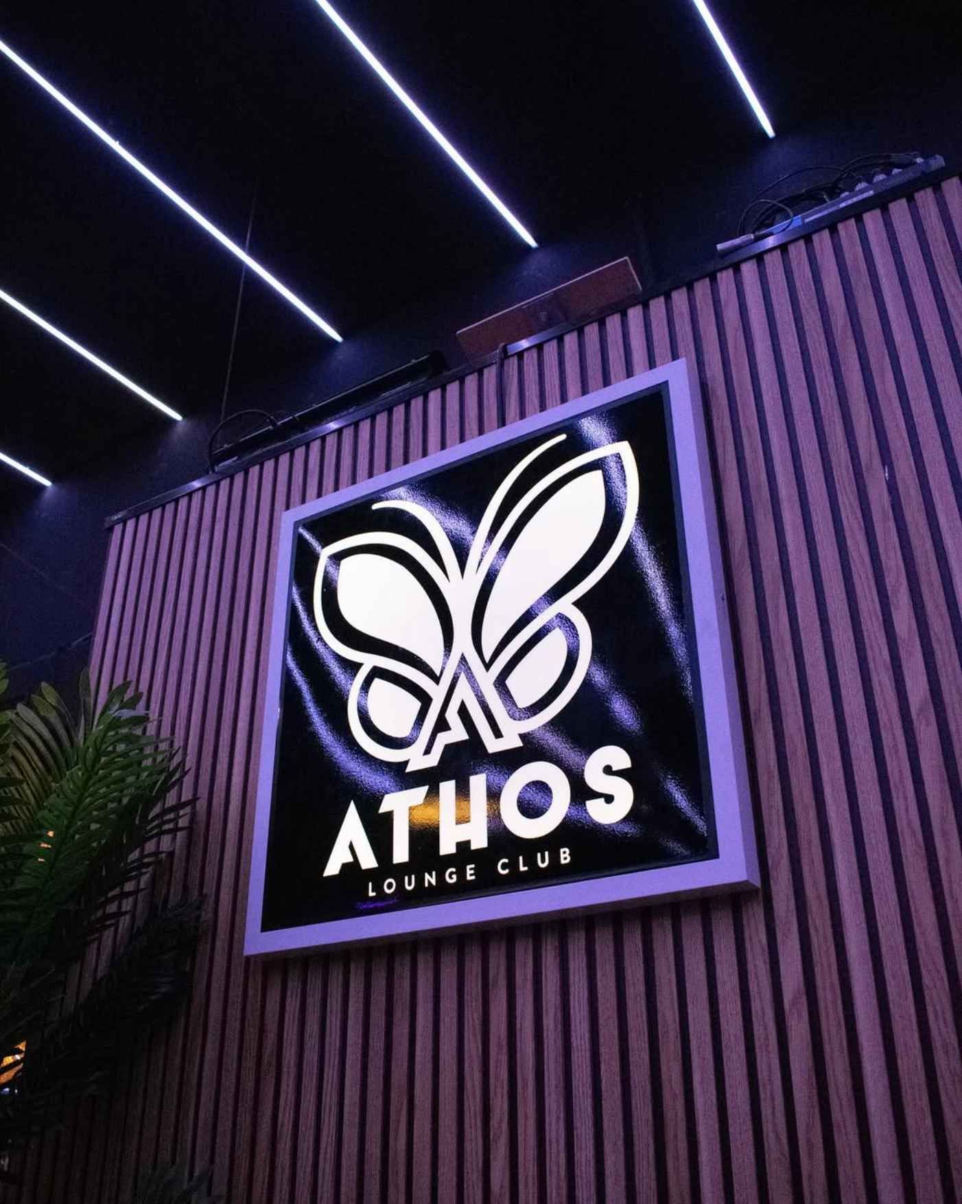 Un cartel del Athos Lounge Club cuelga en una pared de madera.