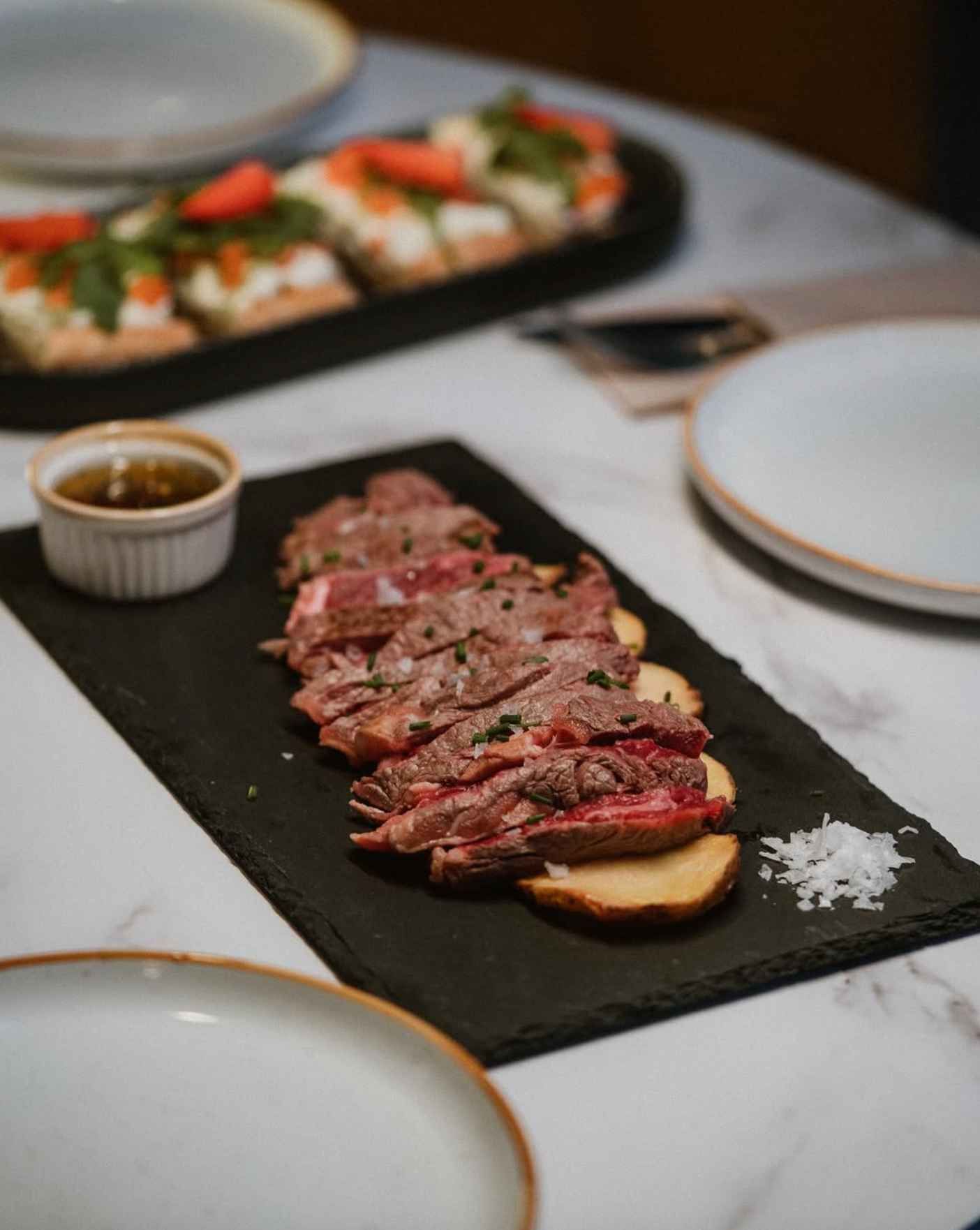 Una tabla de cortar negra cubierta con carne cortada en rodajas y patatas sobre una mesa.