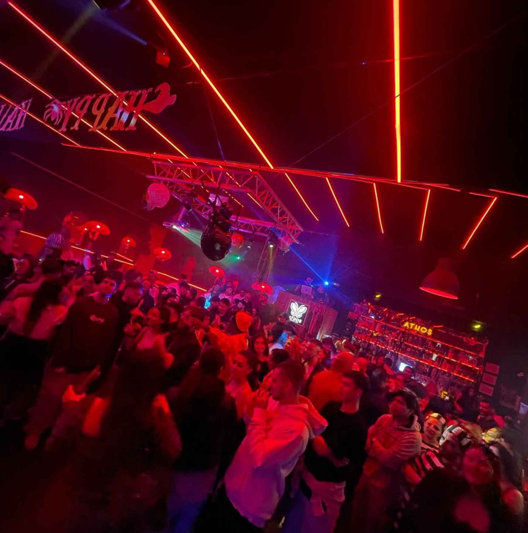 Una multitud de personas baila en una habitación oscura con luces rojas.