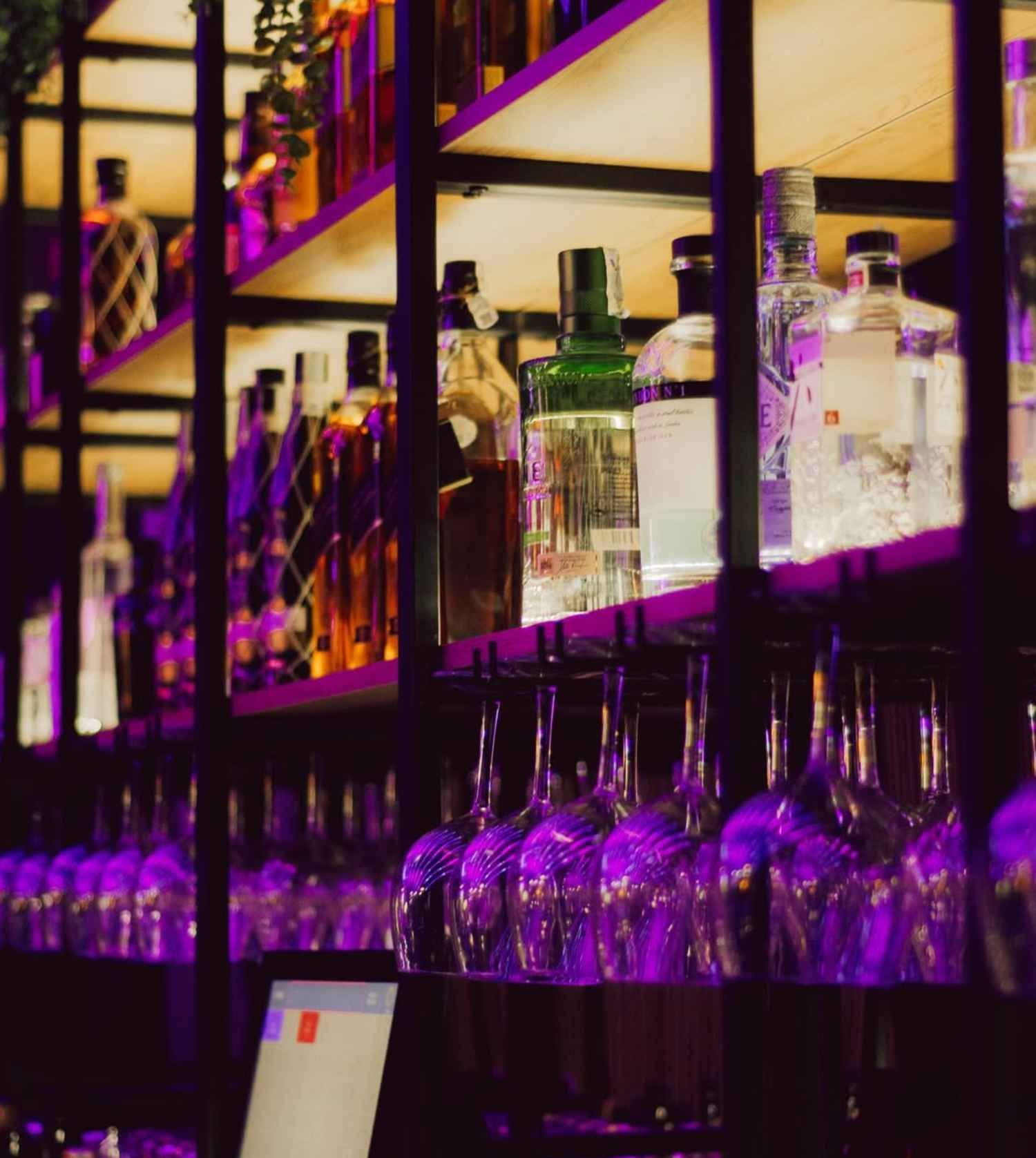 Un bar con muchas botellas y vasos en los estantes.