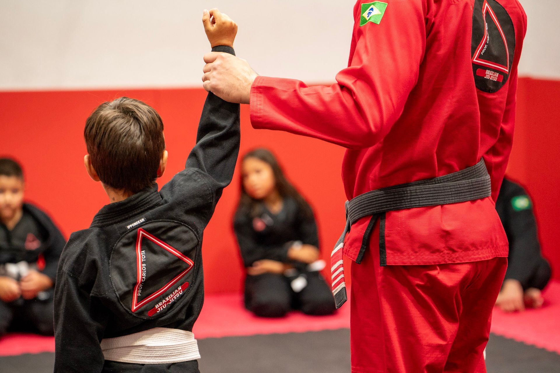 Un hombre con un uniforme de karate rojo le choca los cinco a un niño.
