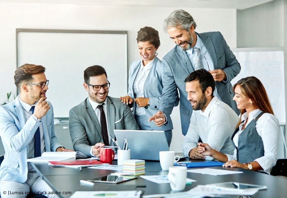 Ein diverses Team in Businesskleidung arbeitet in einem Büro um einen Konferenztisch herum zusammen