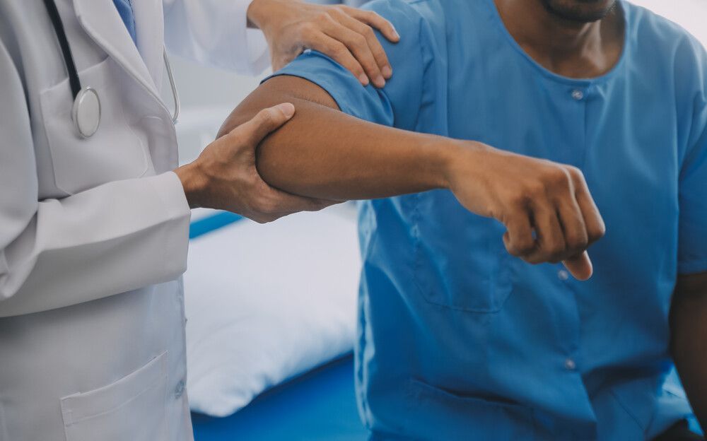 Un médico está examinando el codo de un paciente en una habitación de hospital.