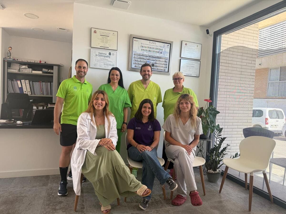 Un grupo de personal médico sonriente con uniformes verdes y de colores claros posa dentro de una clínica.