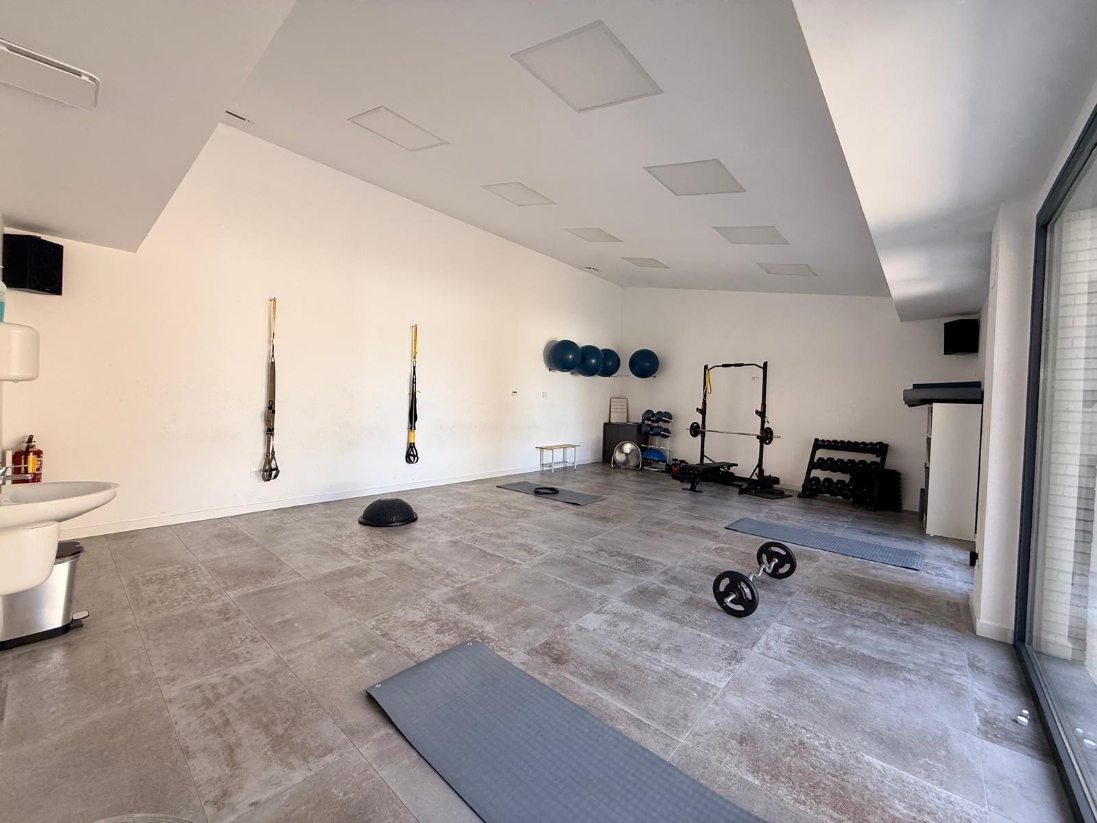 Estudio de entrenamiento luminoso y vacío con colchonetas, mancuernas y equipo de ejercicio sobre un suelo alfombrado.