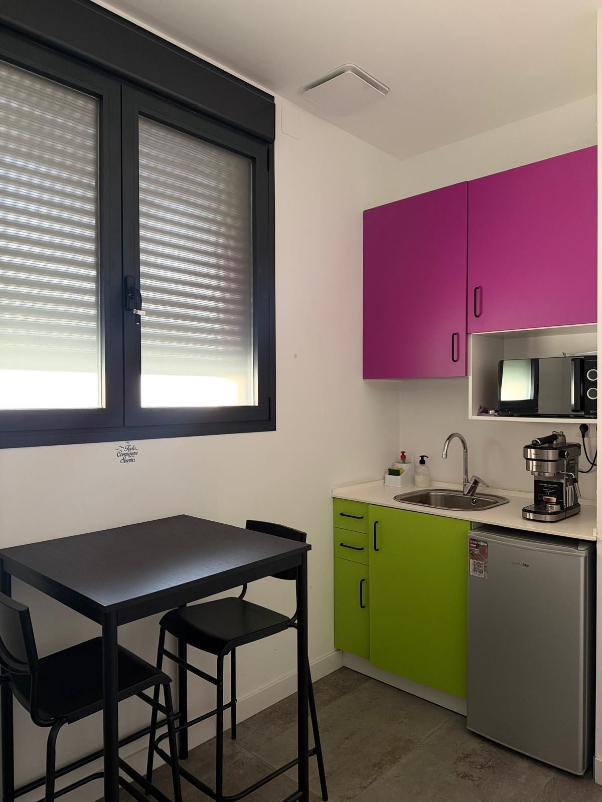Habitación luminosa y minimalista con paredes blancas, escritorio, silla, ventana y suelo de hormigón.