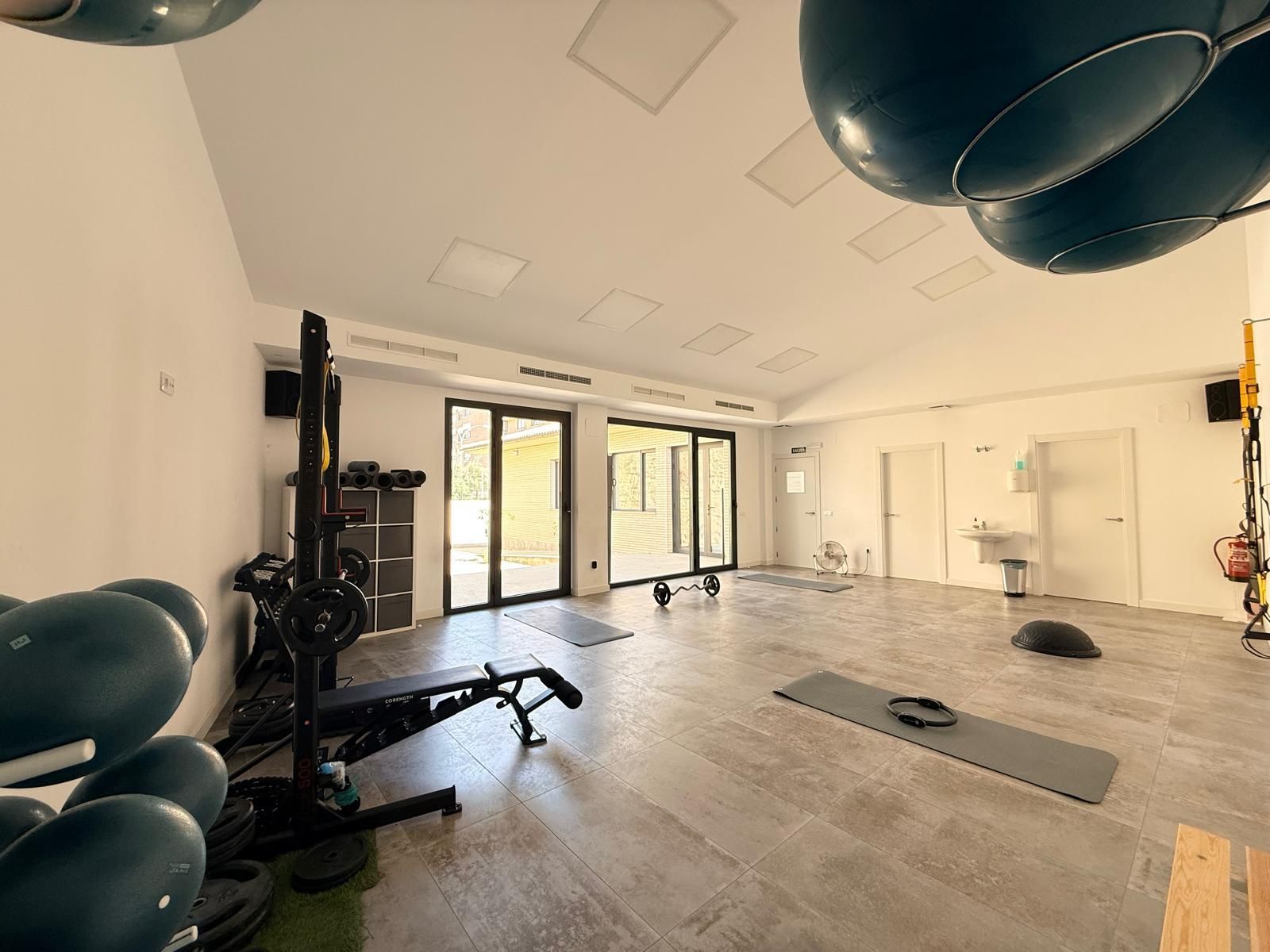 Gimnasio moderno con aparatos de ejercicio, espejos grandes y balones de estabilidad negros sobre un suelo de madera clara.