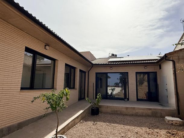 Pequeño patio de ladrillo con suelo de grava, plantas en macetas y puertas correderas de cristal bajo un cielo nublado.