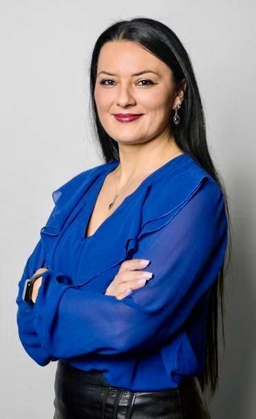 Una mujer con una camisa azul está de pie con los brazos cruzados.