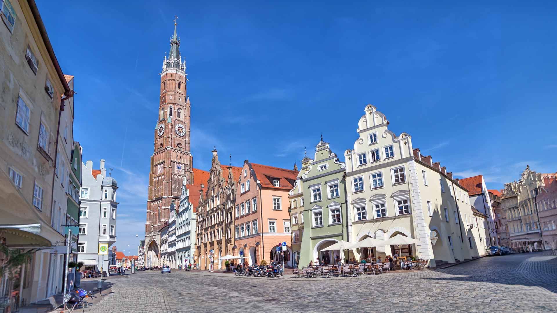 Kopfsteinpflasterstraße mit farbenfrohen Gebäuden und einem hohen Uhrturm unter blauem Himmel.