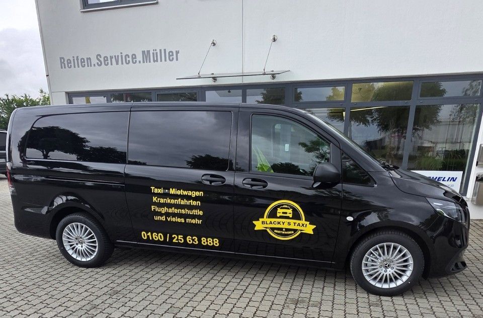 Ein schwarzer Lieferwagen parkt vor einem Gebäude mit Text und Logo an der Seite.