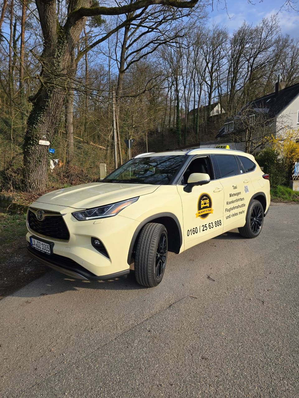 Ein gelbes Toyota Highlander Taxi parkt auf einer Straße neben Bäumen und einem Gebäude.