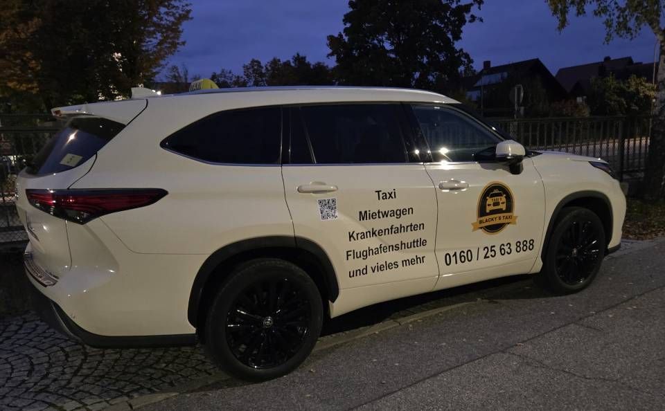 Weißes SUV-Taxi mit schwarzen Felgen; Aufschrift auf der Tür: Taxi, Telefonnummer, QR-Code.