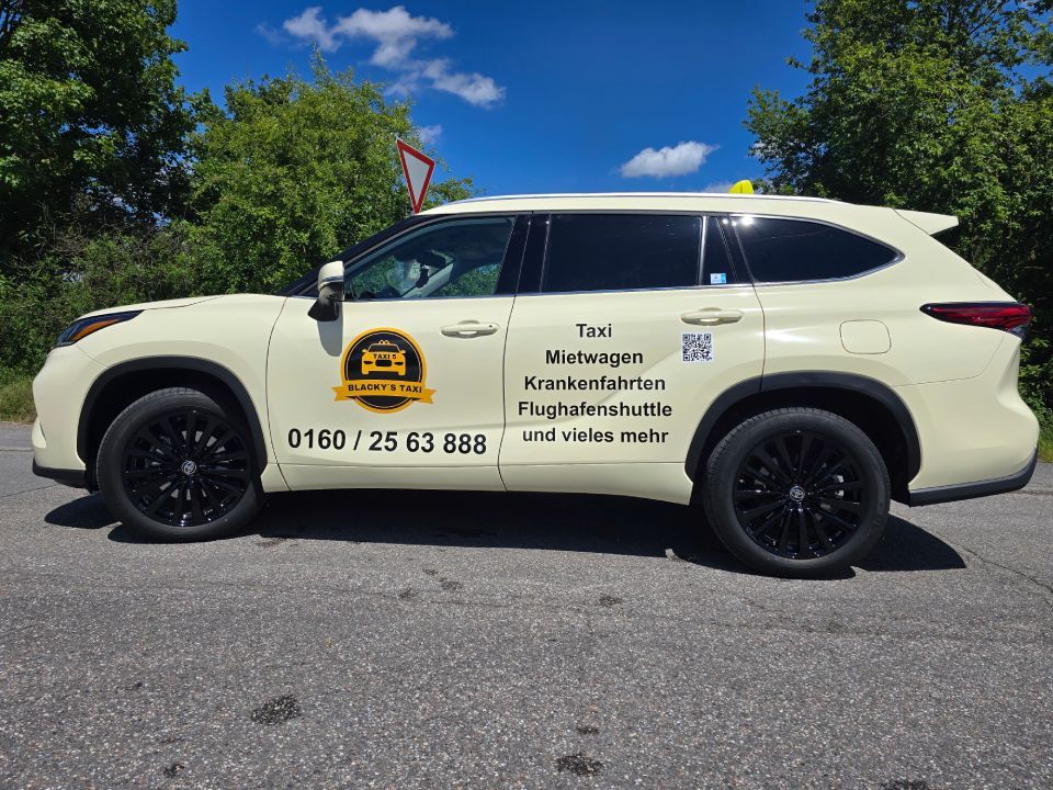 Ein beiges Taxi mit schwarzen Rädern auf einer Straße, das für seine Dienstleistungen wirbt, vor blauem Himmel.