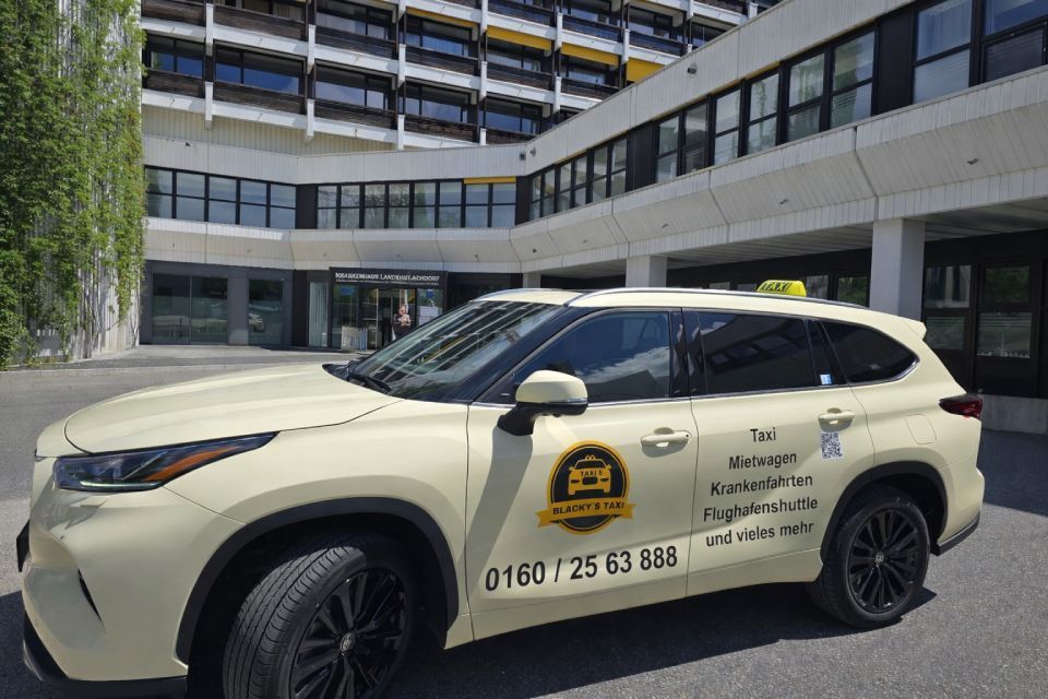 Ein beiges Taxi parkte vor einem modernen Gebäude mit viel Grün.