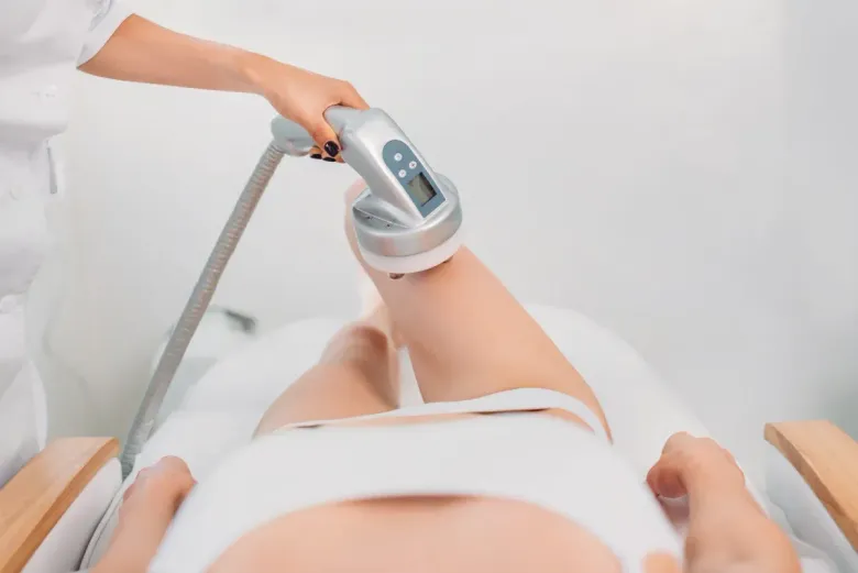 En un entorno clínico y de color blanco, un profesional utiliza un dispositivo cosmético manual en la pierna de una persona.