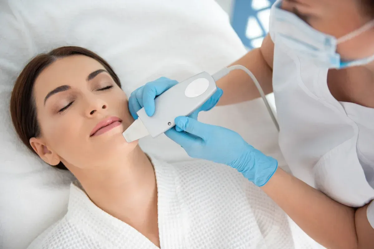 Un profesional, con mascarilla y guantes, utiliza un dispositivo cosmético manual en la barbilla