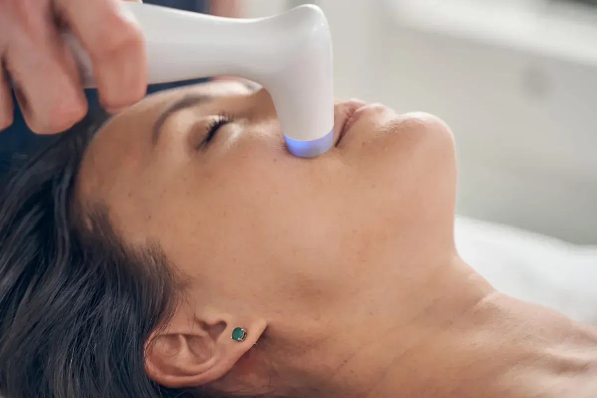 Una persona que recibe un tratamiento de fototerapia cosmética en el rostro mediante un dispositivo portátil.