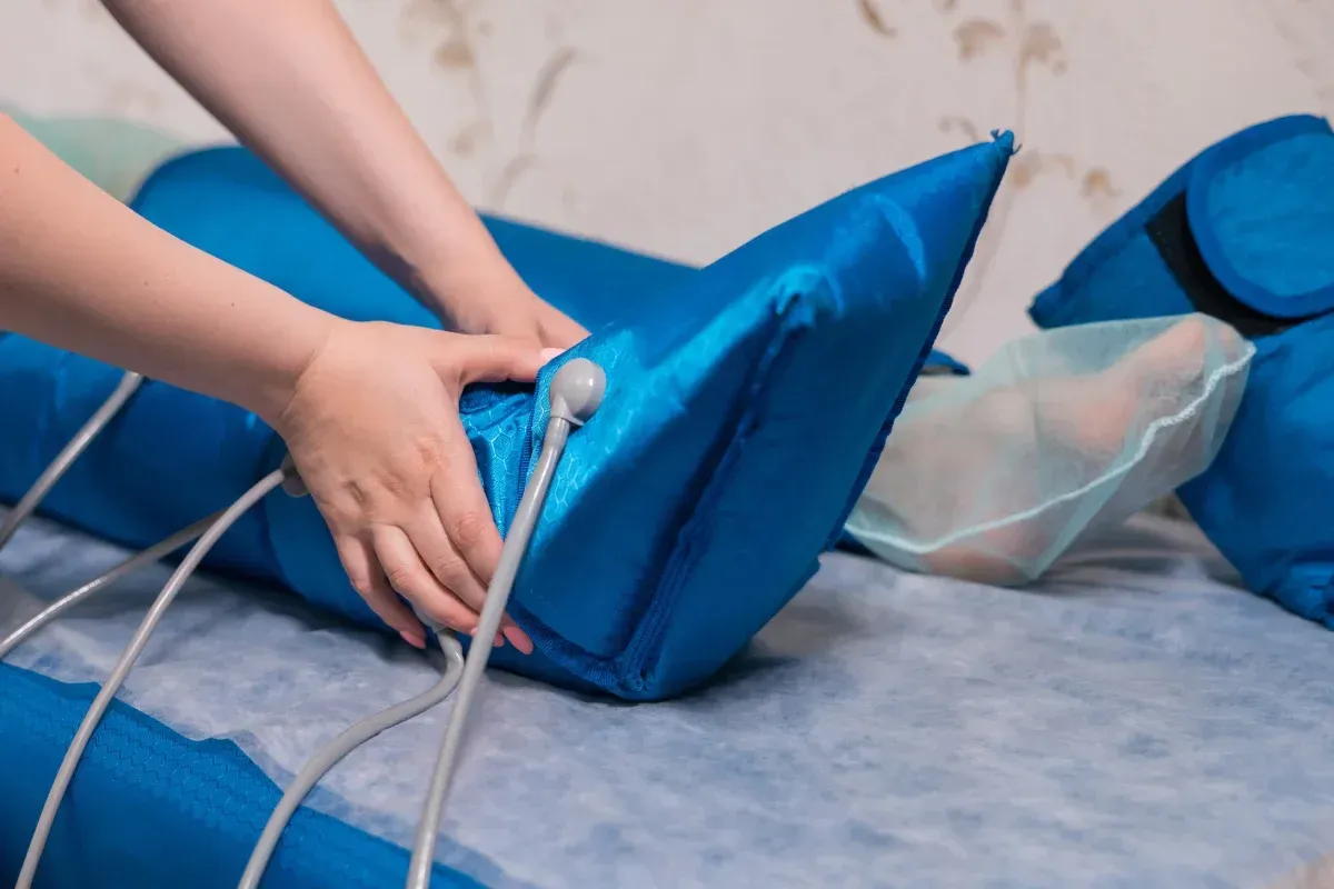 Durante una sesión de fisioterapia, una persona ajusta con sus manos una manga de compresión neumática azul