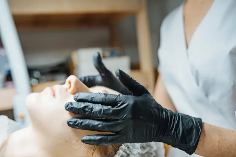 Una persona con guantes negros realiza un masaje facial a un cliente que está tumbado en un spa profesional.