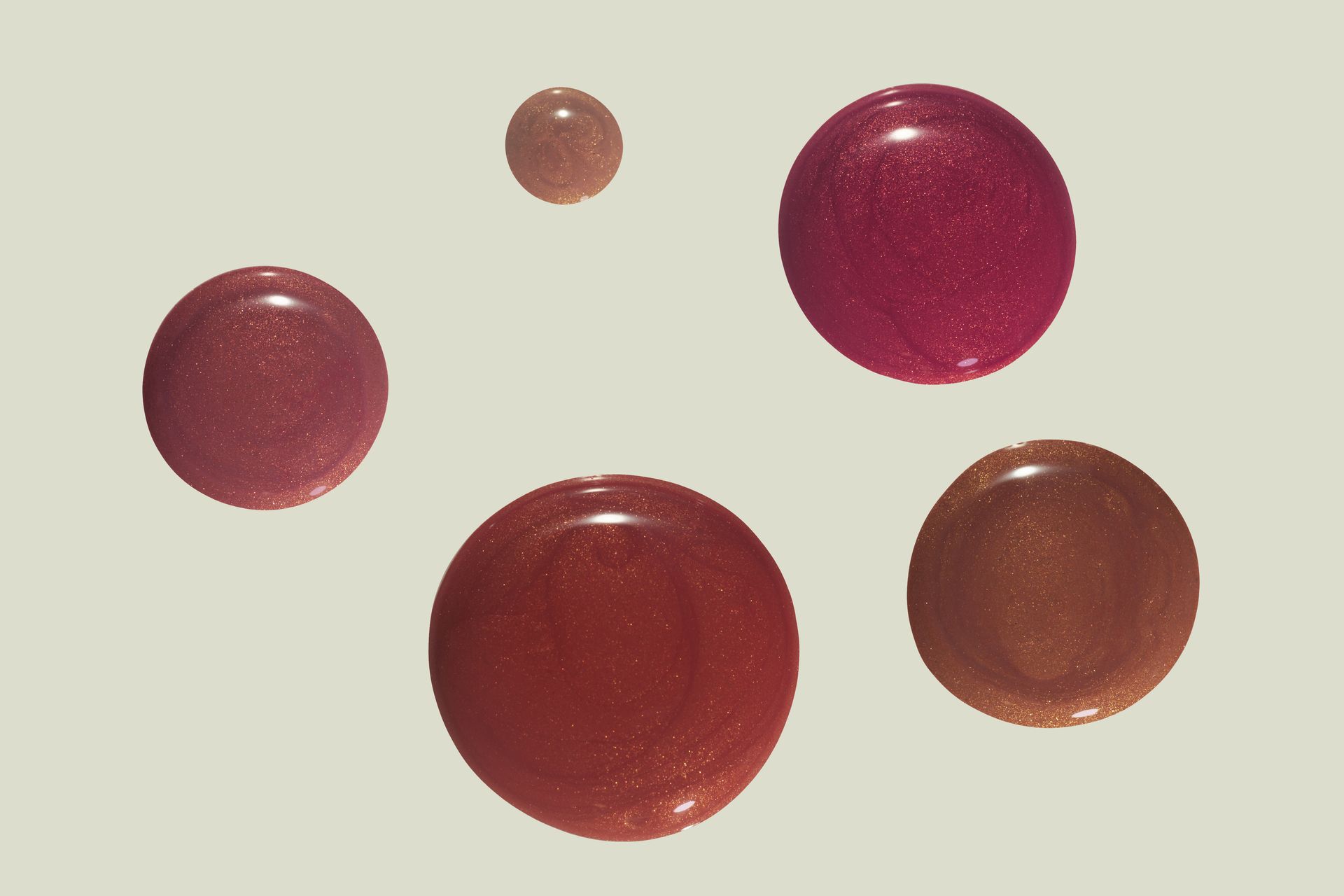 Cinq gouttelettes de vernis irisées, brun rougeâtre sur un fond beige clair.