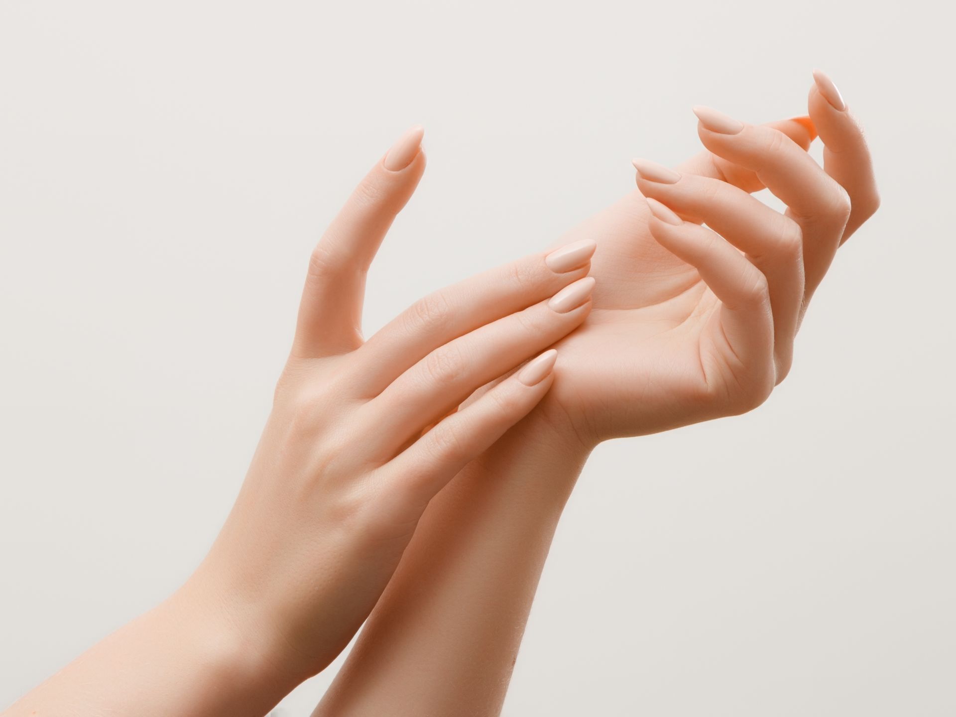 Deux mains, peau pâle, se touchant avec de longs ongles clairs sur un fond blanc.