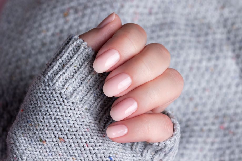 Main aux ongles ovales rose clair posée sur un pull en tricot gris.