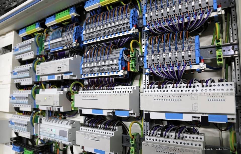 Elektrisches Bedienfeld mit Kabeln, Anschlüssen und Geräten, die an einer Wand montiert sind.