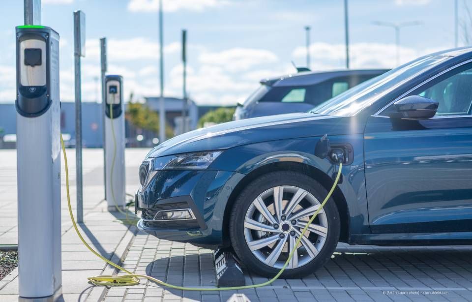 Blaues Elektroauto wird an einer Station aufgeladen, Sonnenlicht wird vom Auto reflektiert.