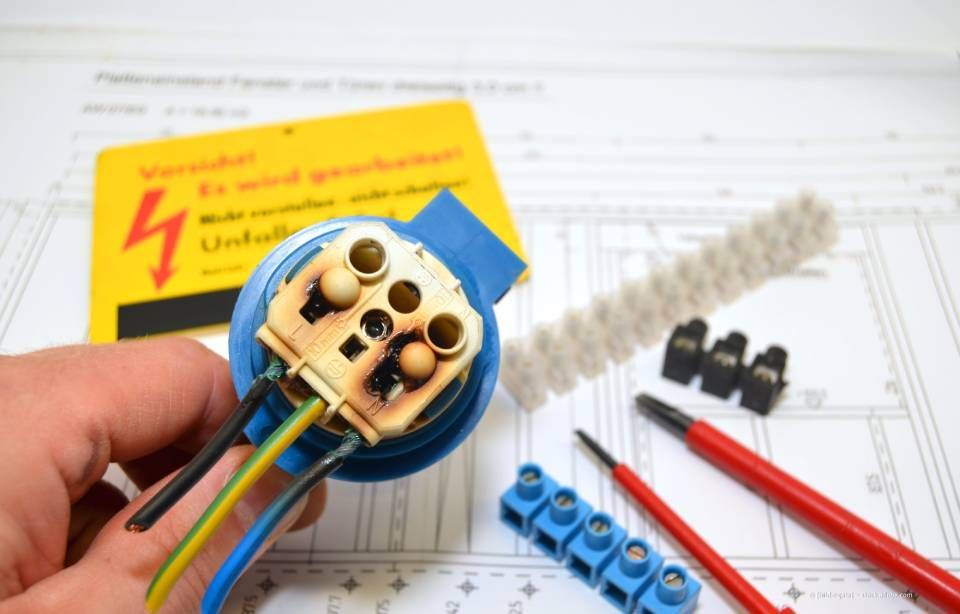 Durchgebrannter elektrischer Stecker mit Kabeln, Werkzeugen und Warnschild.