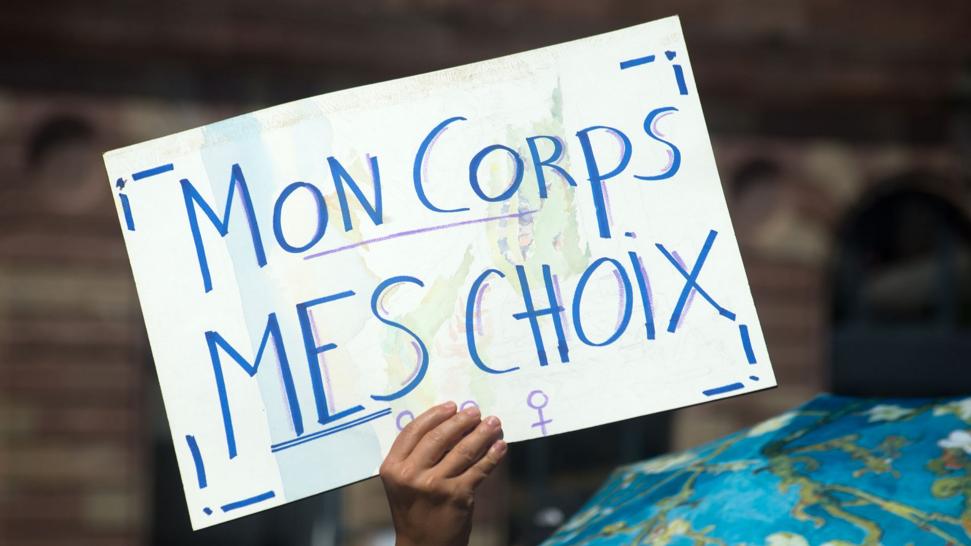 Main tenant une pancarte sur laquelle on peut lire 'Mon corps, mes choix' en français.