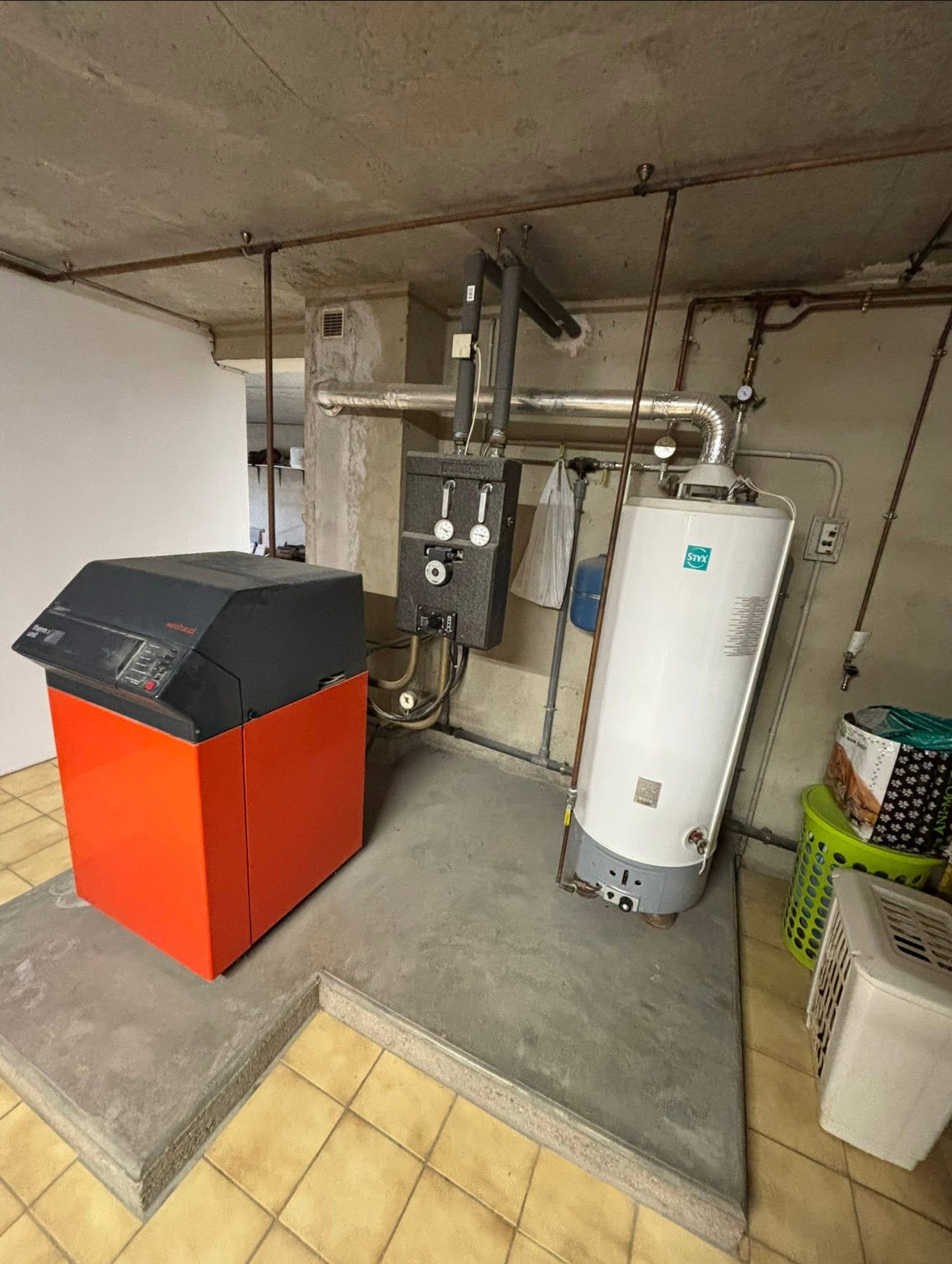 Système de chauffage dans un sous-sol avec une chaudière rouge et noire, un chauffe-eau et des tuyaux.