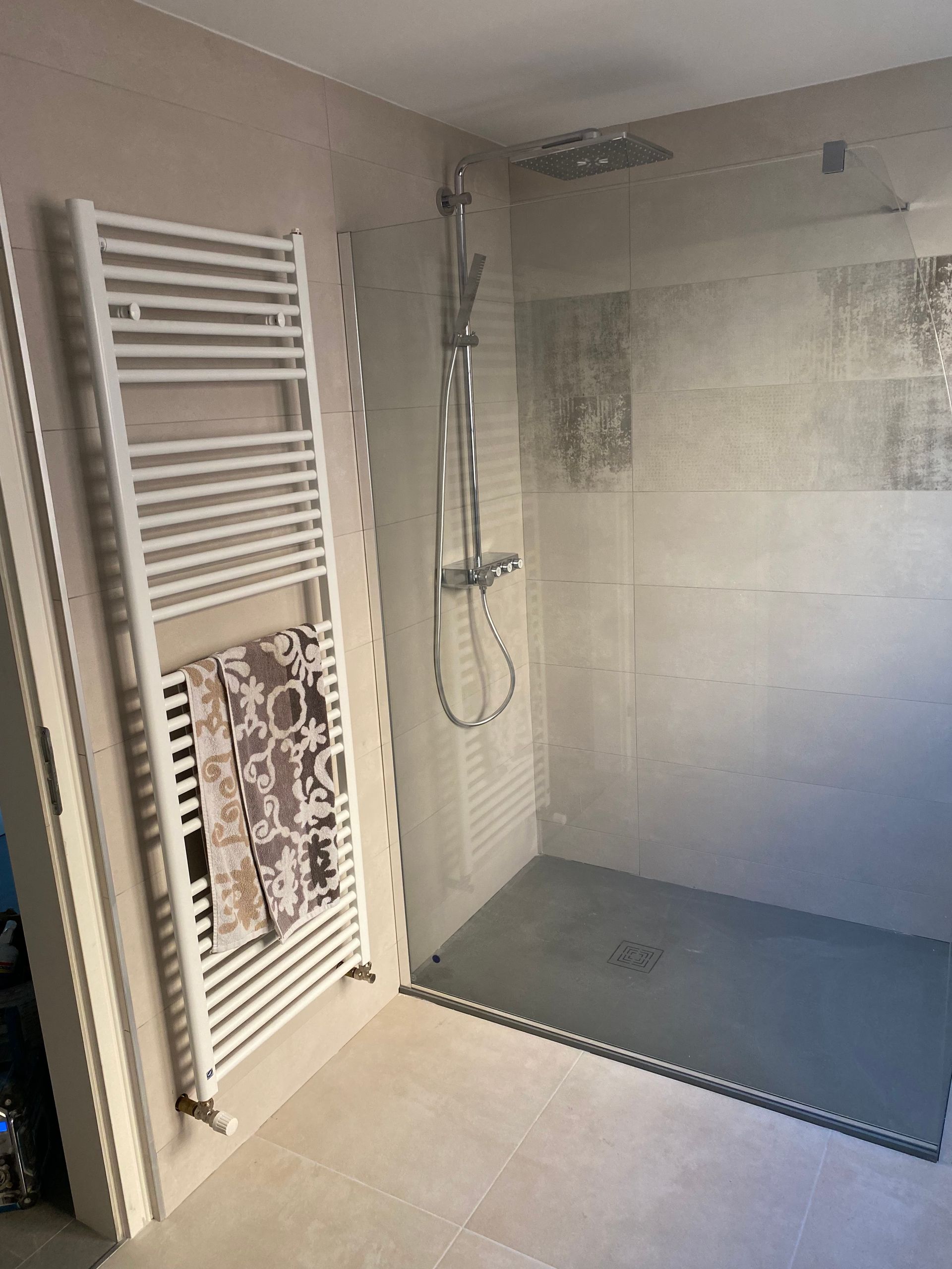 Salle de bains avec sèche-serviettes blanc, douche à l'italienne avec sol gris, carrelage et murs de couleur claire.