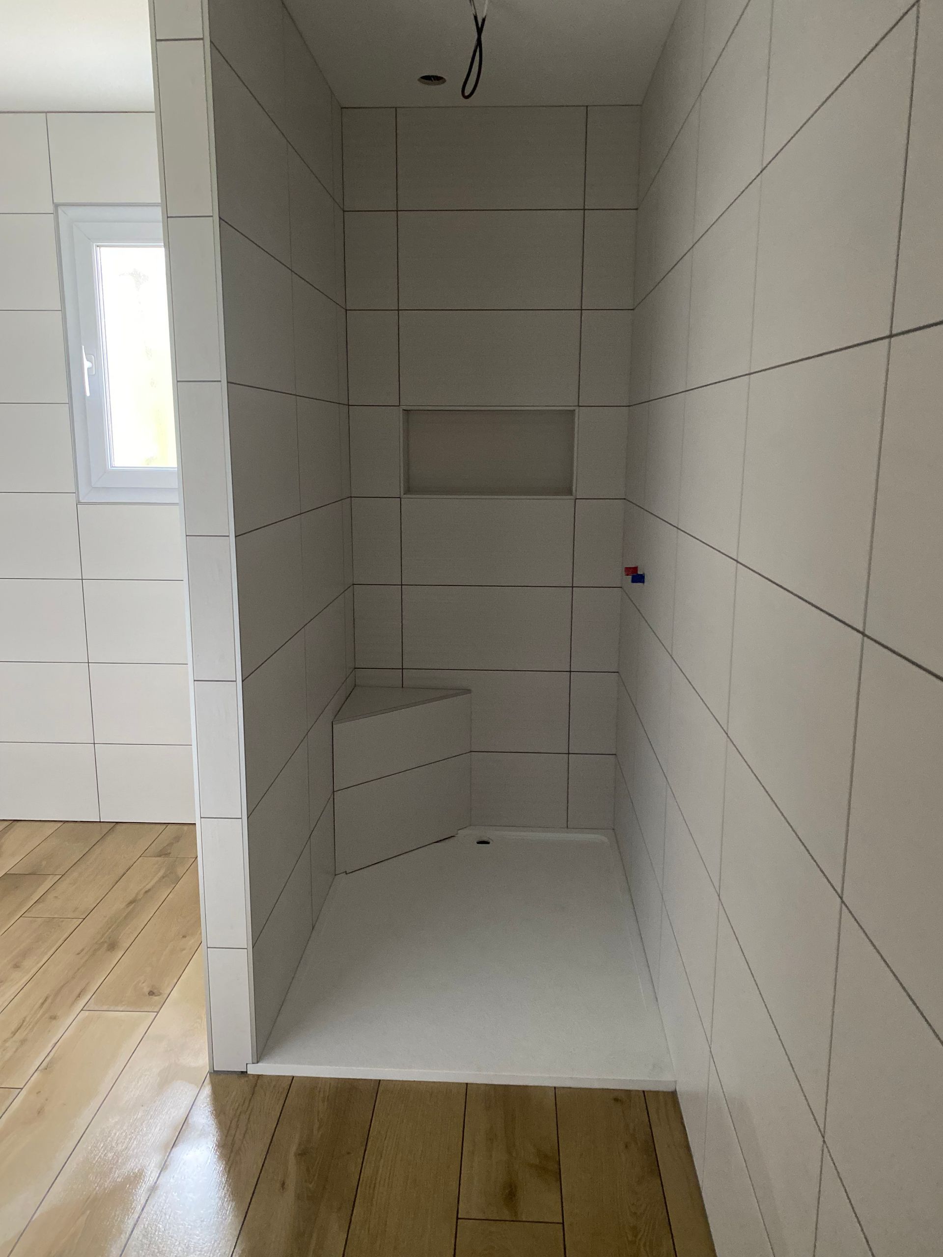 Cabine de douche blanche en cours d'aménagement avec siège d'angle et niche. Sol en bois brun.