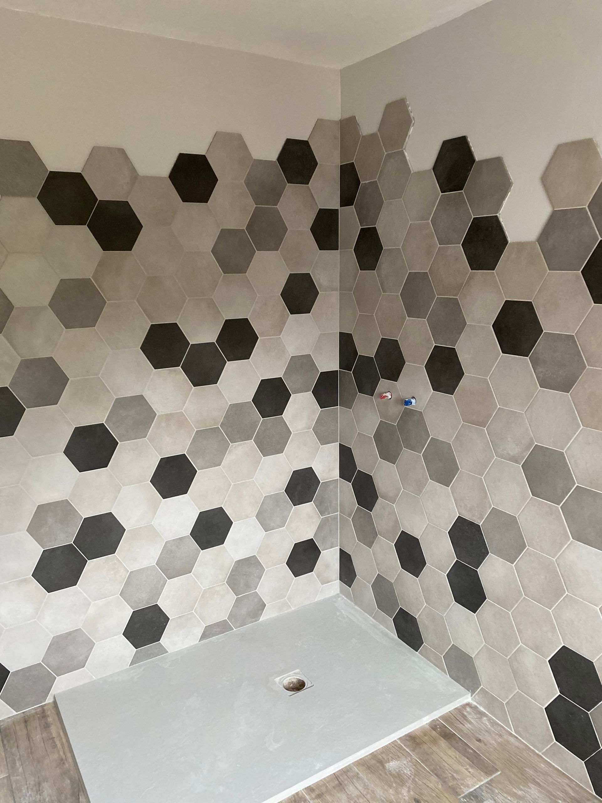 Cabine de douche avec carrelage hexagonal dans les tons de gris et de noir, plafond blanc et sol gris.