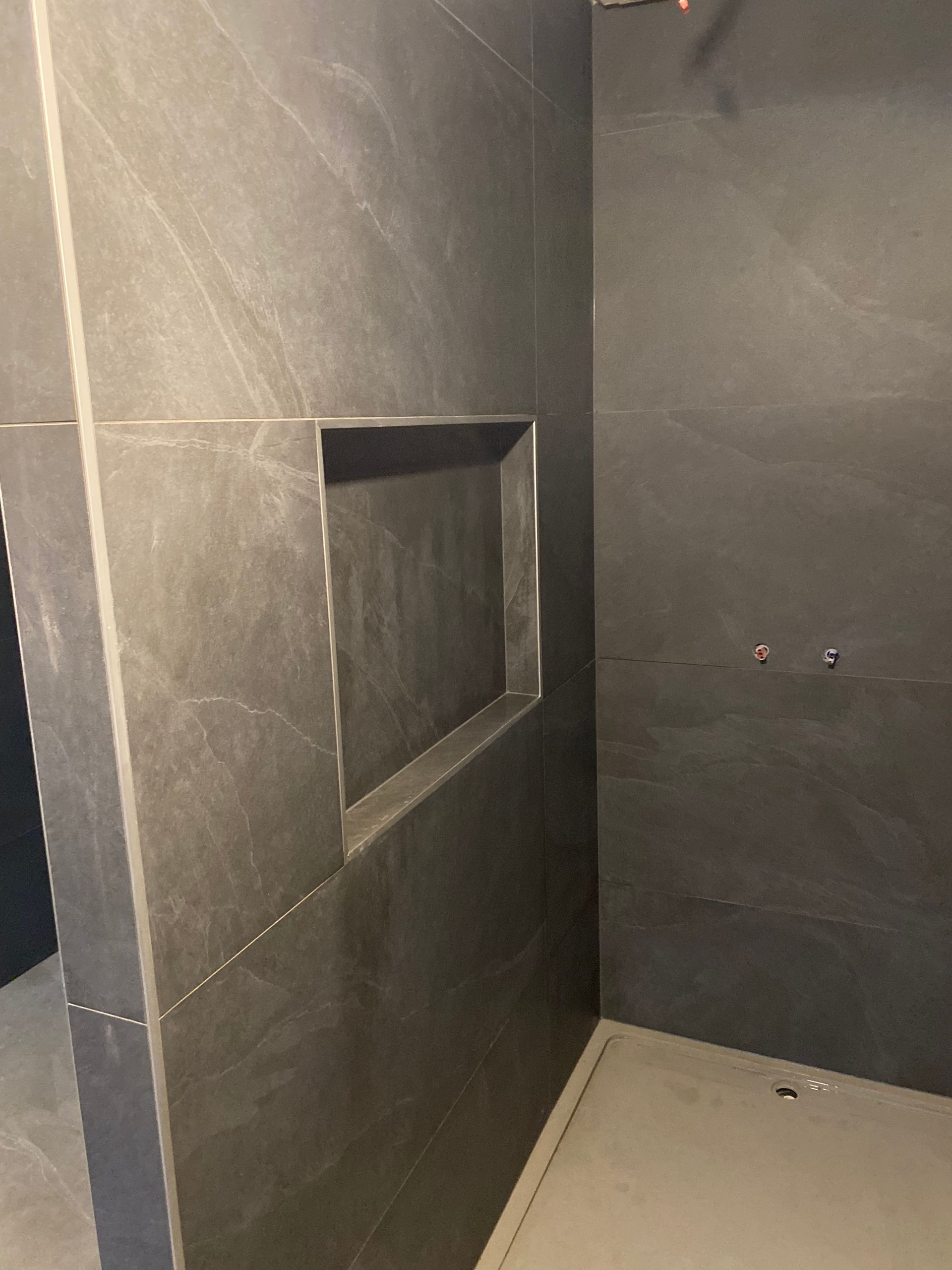 Douche carrelée grise avec étagère encastrée intégrée.