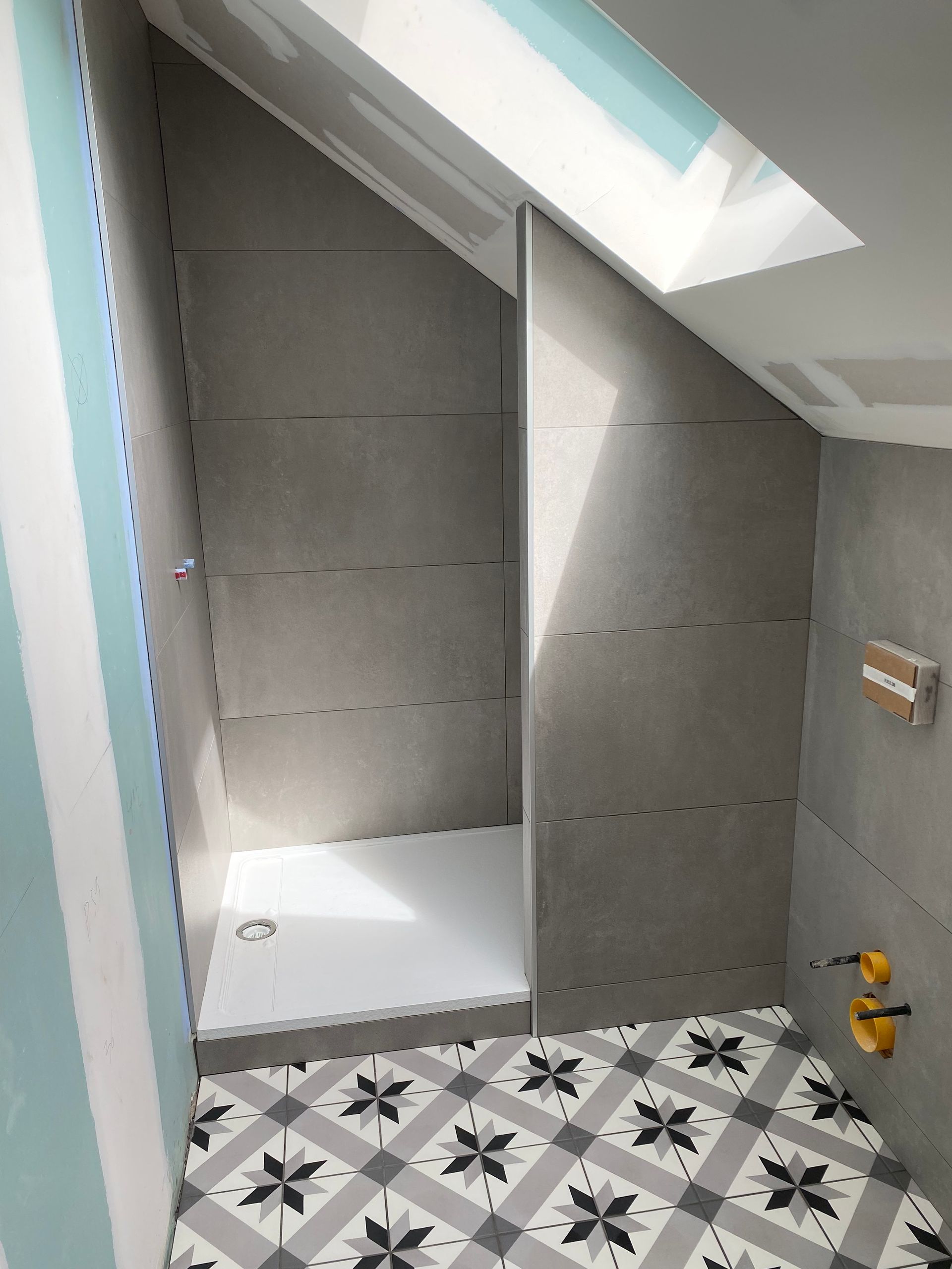 Salle de bains avec murs en biais, douche, carrelage à motifs au sol et puits de lumière.