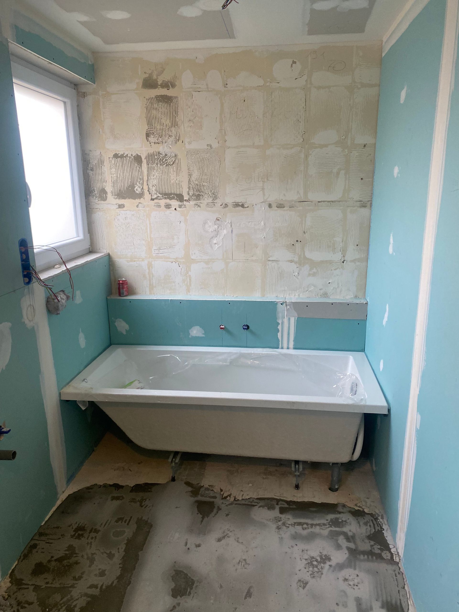 Rénovation de salle de bain en cours, avec baignoire, cloisons sèches bleues et pans de murs apparents.