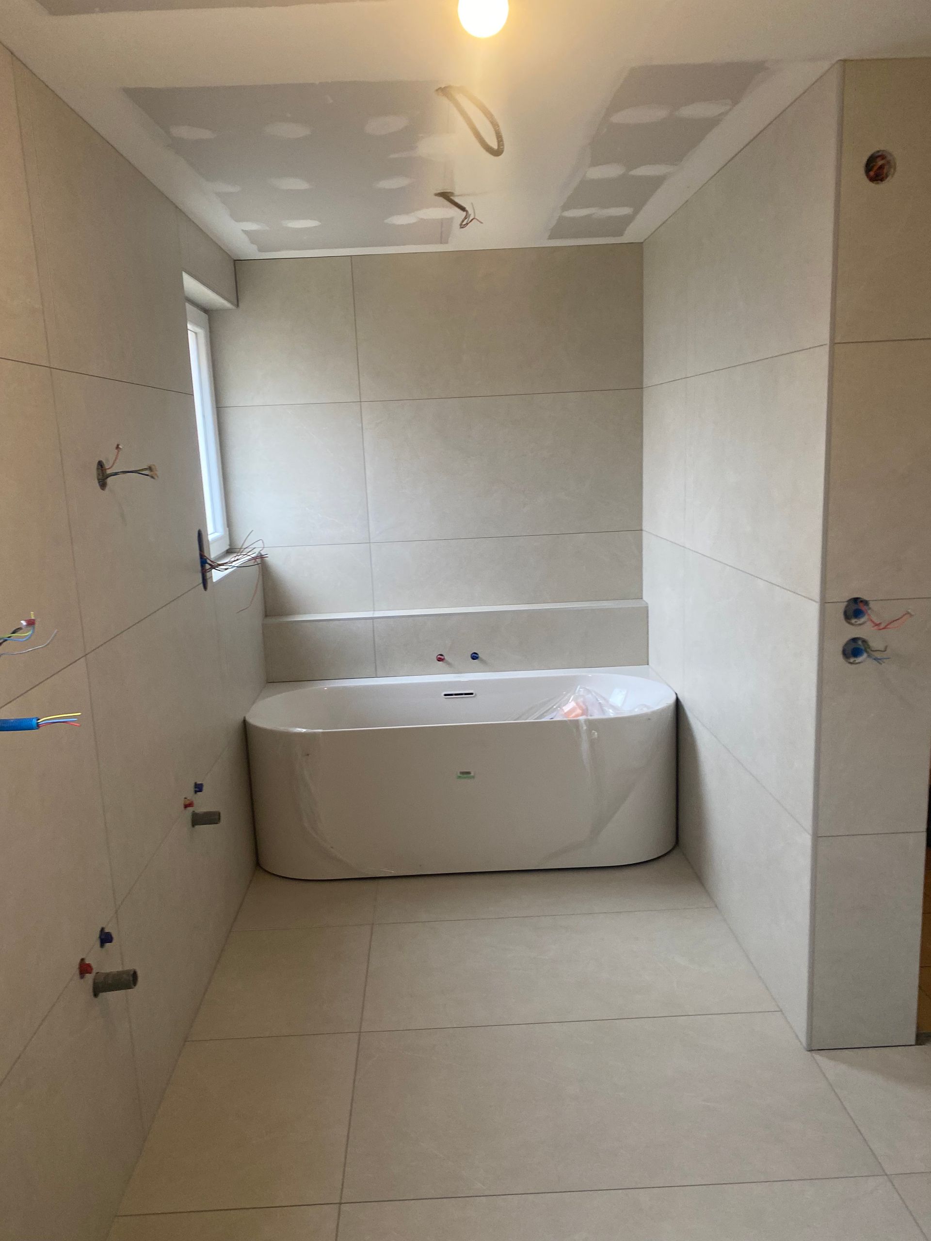 Salle de bains en construction avec carrelage blanc, baignoire et plafond partiellement fini.