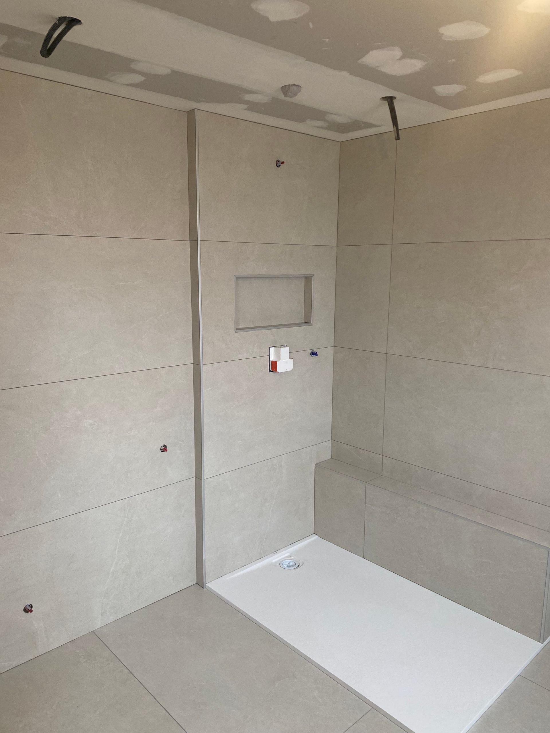 Salle de bains en construction ; murs gris et receveur de douche blanc.