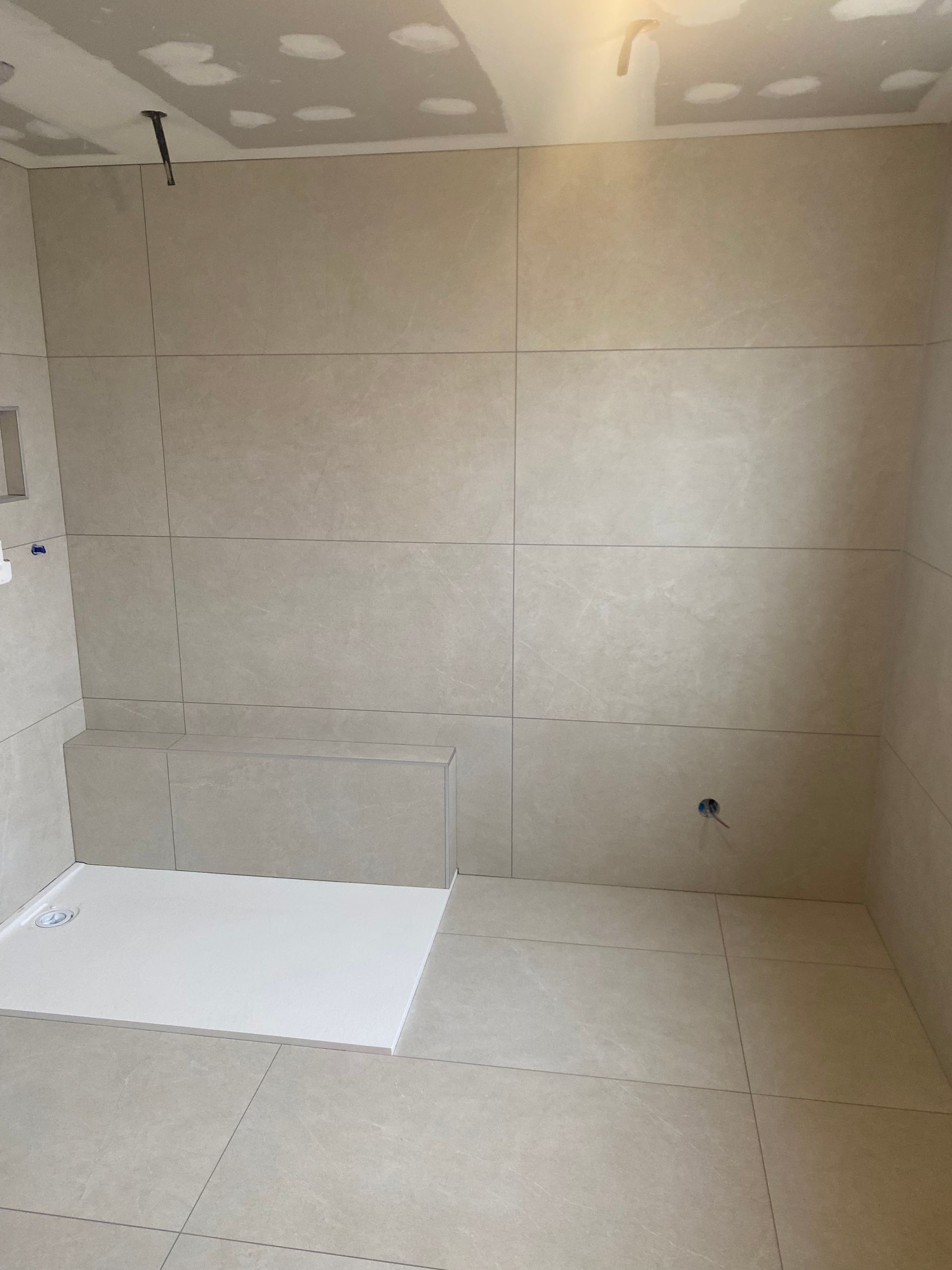 Salle de bains en construction avec murs et panneaux de sol beiges, receveur de douche blanc.