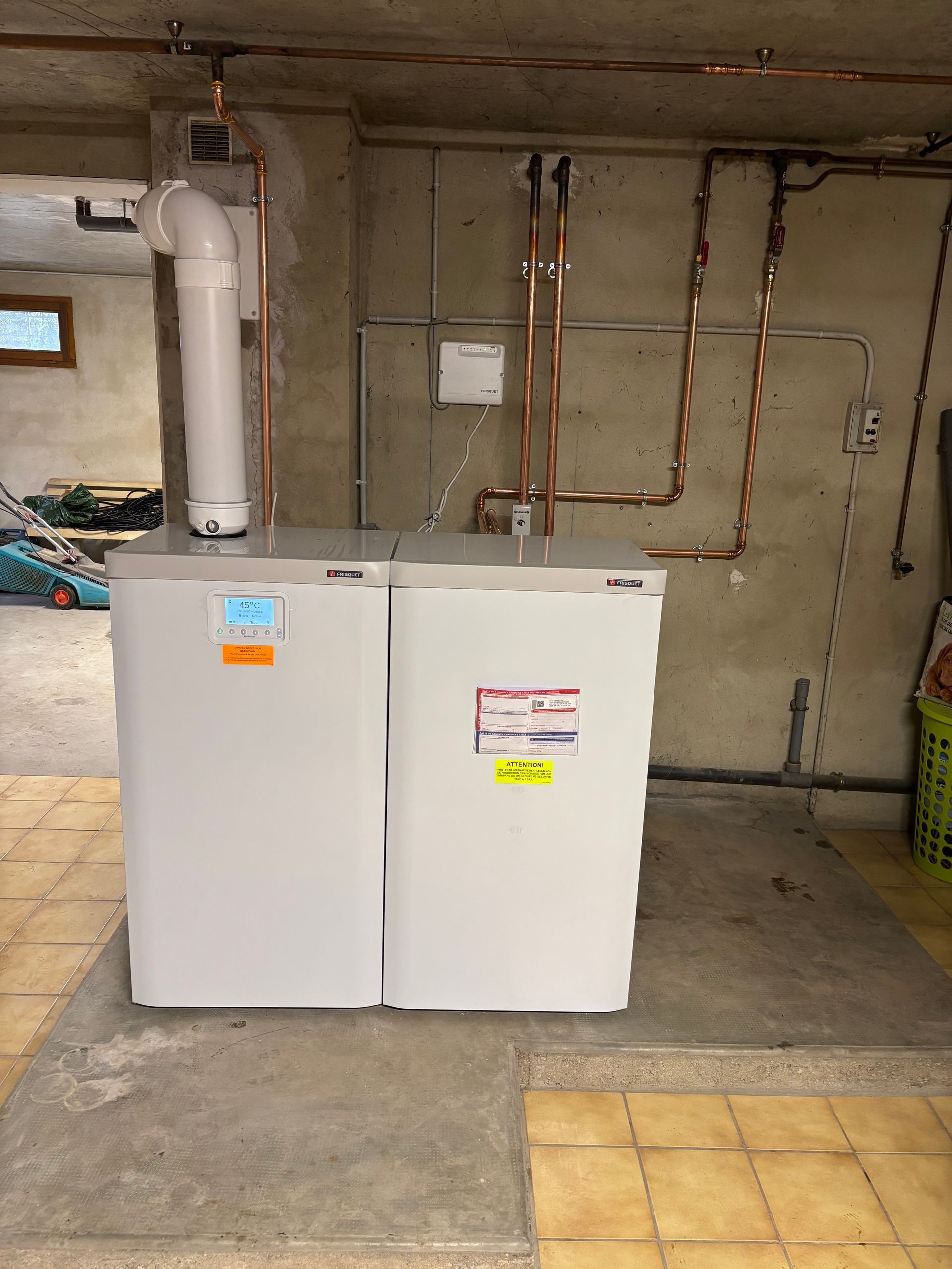 Chaudière blanche dans un sous-sol, des tuyaux en cuivre au mur.