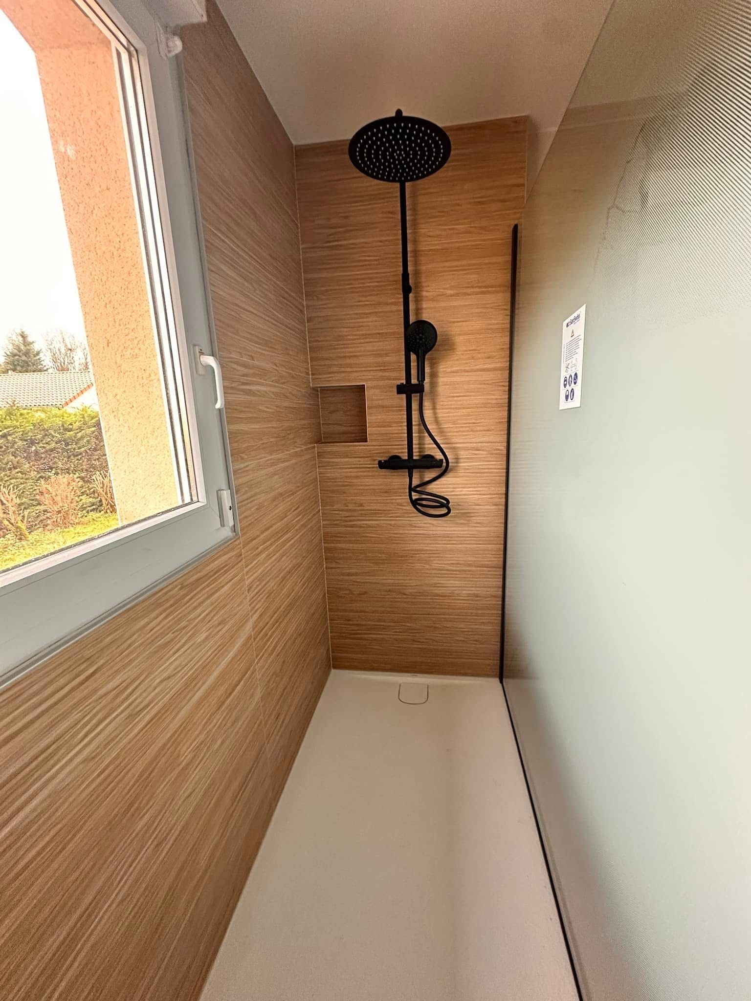 Douche avec robinetterie noire, mur marron clair et sol blanc. Fenêtre à gauche, mur vert clair à droite.