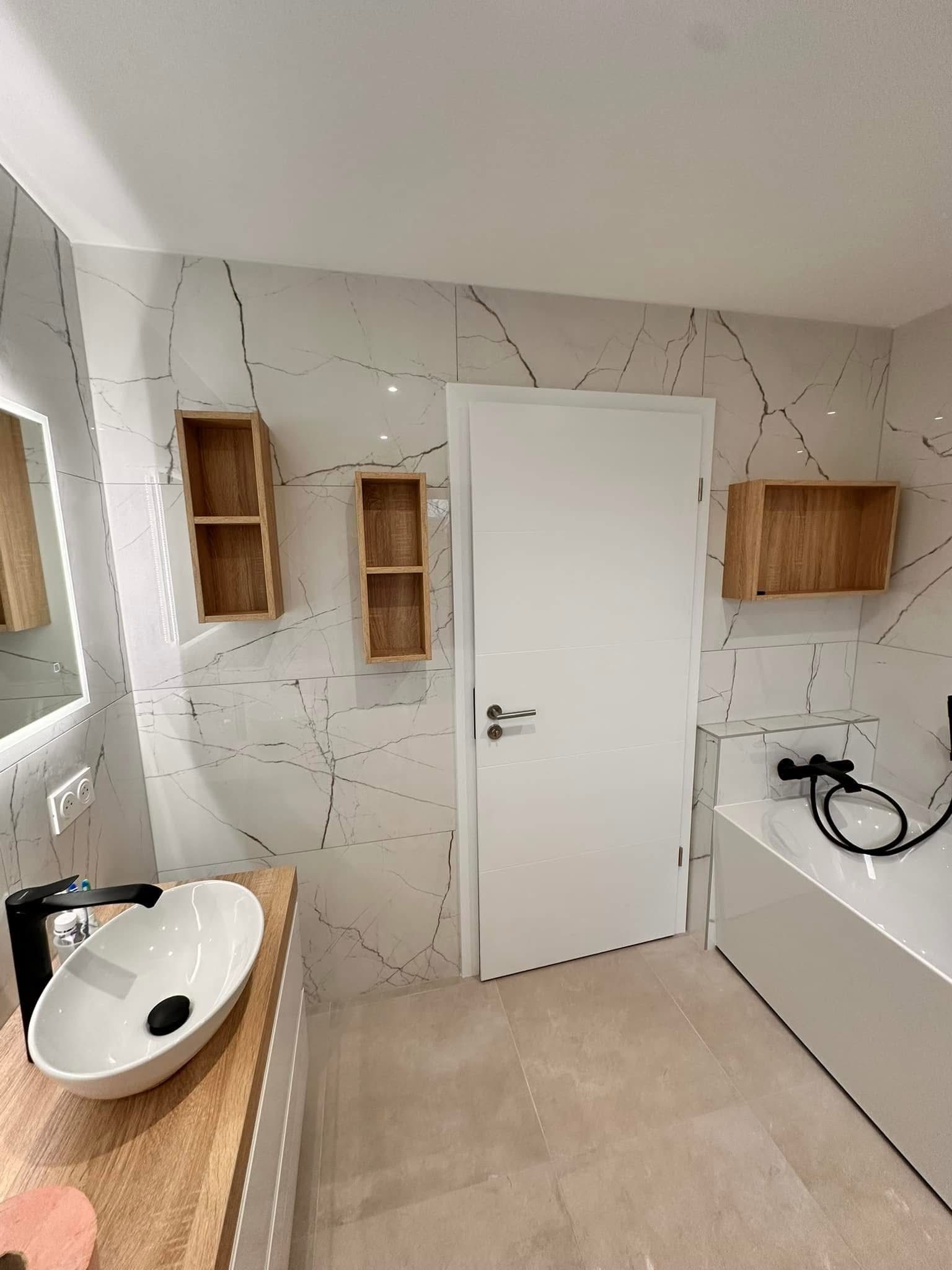 Salle de bains moderne avec murs blancs et en marbre, étagères en bois et porte blanche.