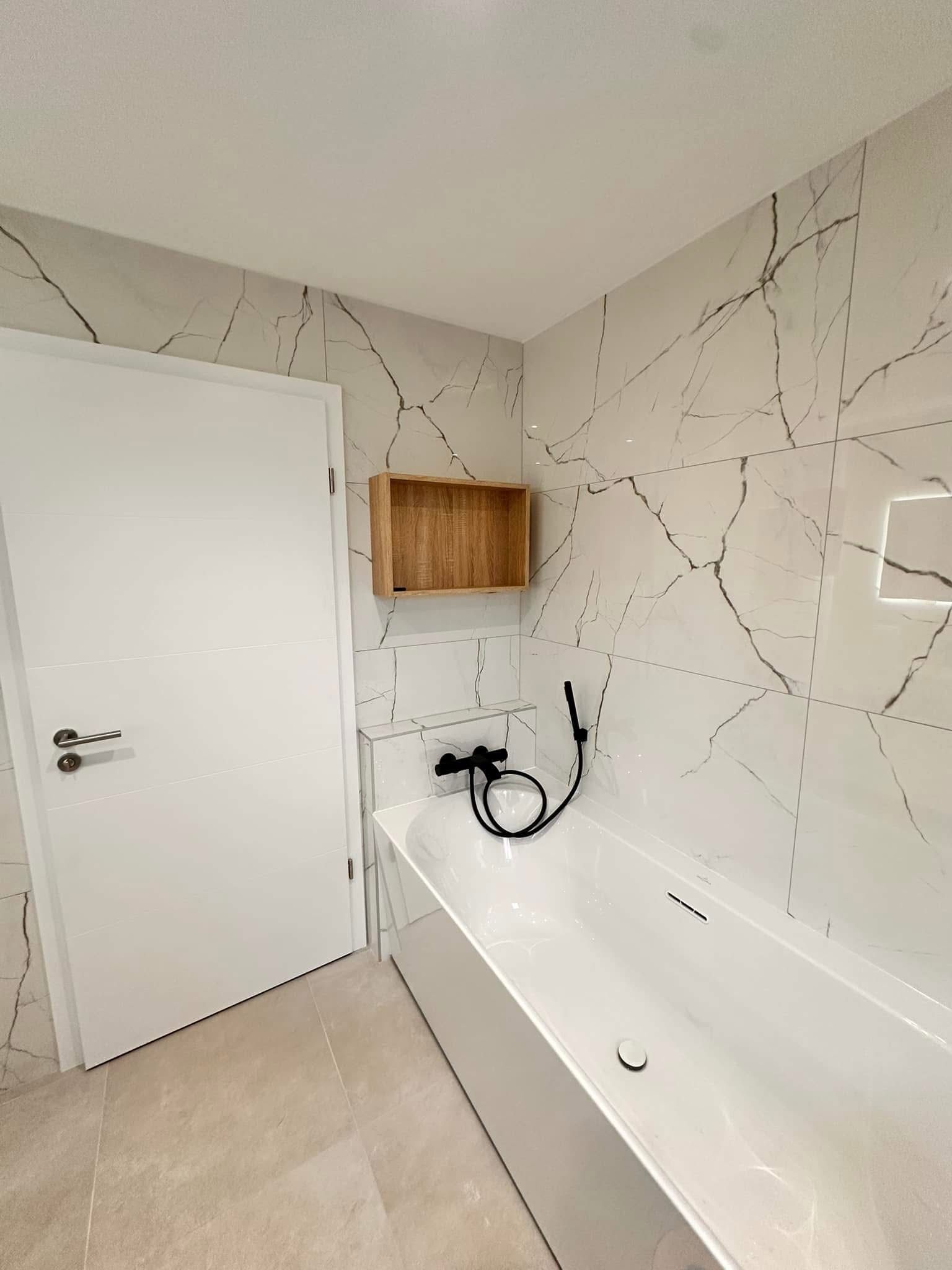 Salle de bains moderne avec murs blancs, baignoire et porte blanche ; carrelage à motif marbre, meuble en bois.