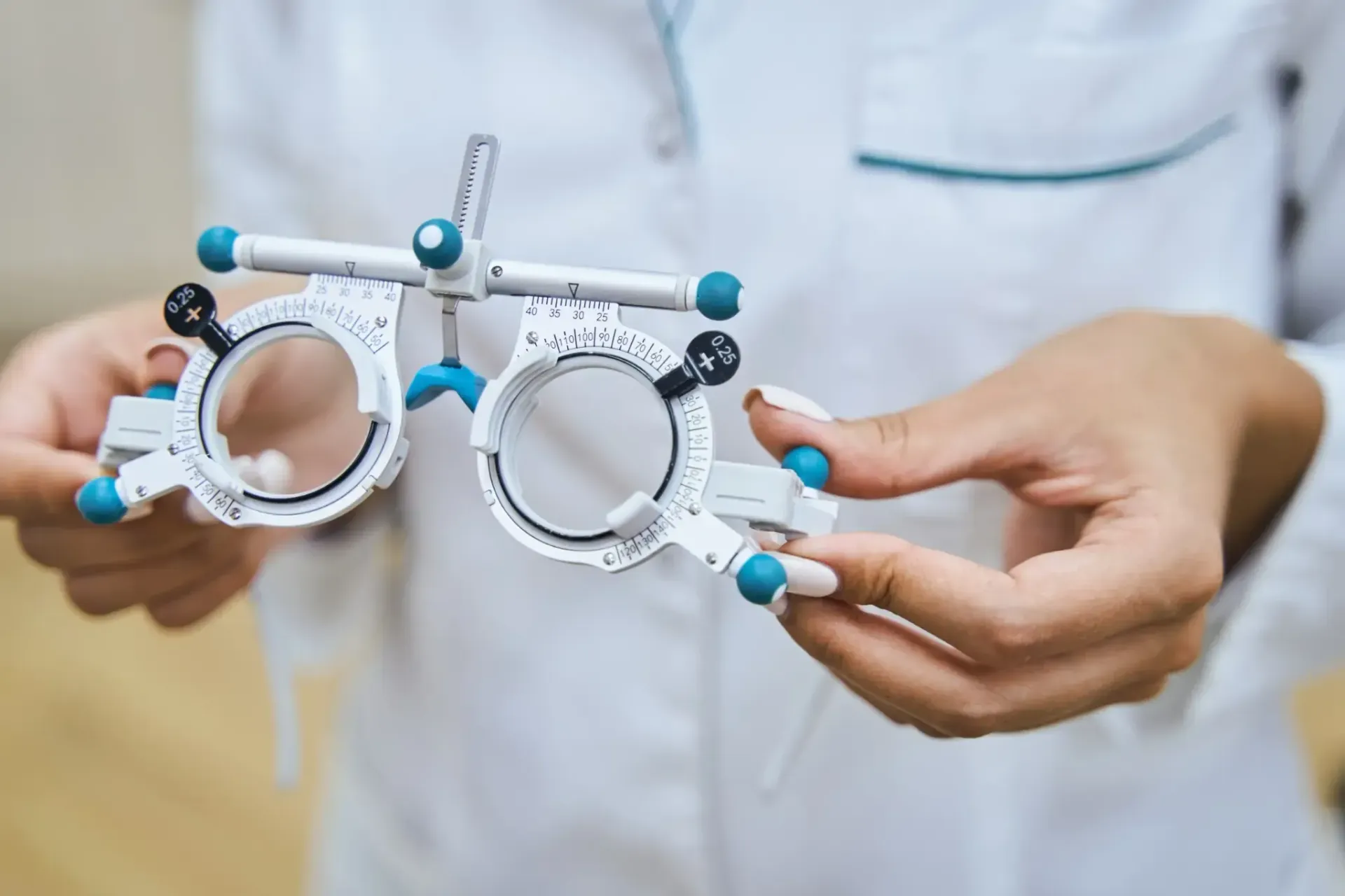 Persona sosteniendo una montura de prueba oftálmica blanca con lentes ajustables.