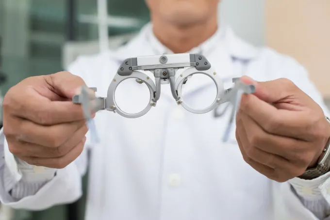 Optometrista sosteniendo un foróptero, un dispositivo utilizado para evaluar la visión, en un entorno clínico.