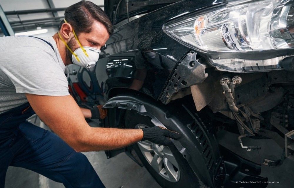 Ein Mechaniker mit Maske inspiziert in einer Garage das Vorderrad eines Autos.