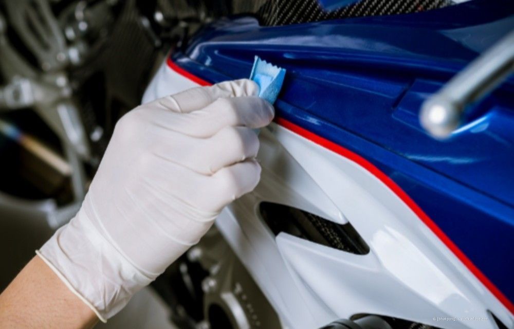 Eine behandschuhte Hand wischt mit einem Tuch die blaue, weiße und rote Motorradverkleidung ab.
