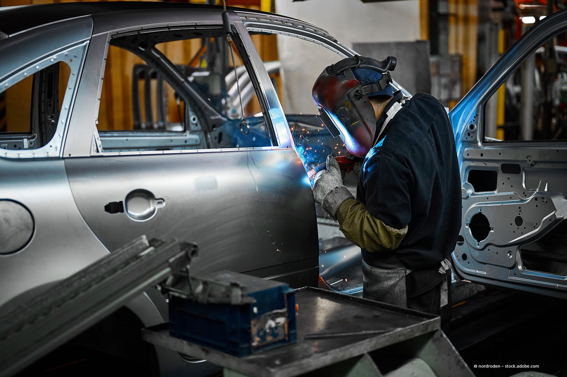 Behandschuhte Hände benutzen einen Schraubenschlüssel, um an einer Autotürschwelle auf einer Metallbodenplatte zu arbeiten.